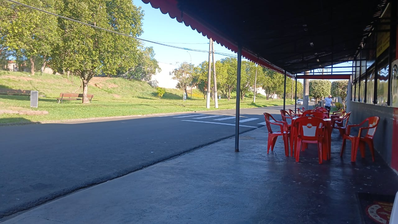 Área externa coberta do boteco com mesas e cadeiras vermelhas